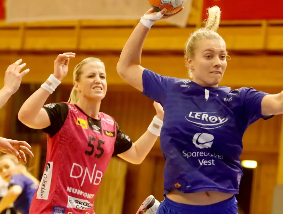 Håndballspiller i blå drakt i hopp med ballen mot mål